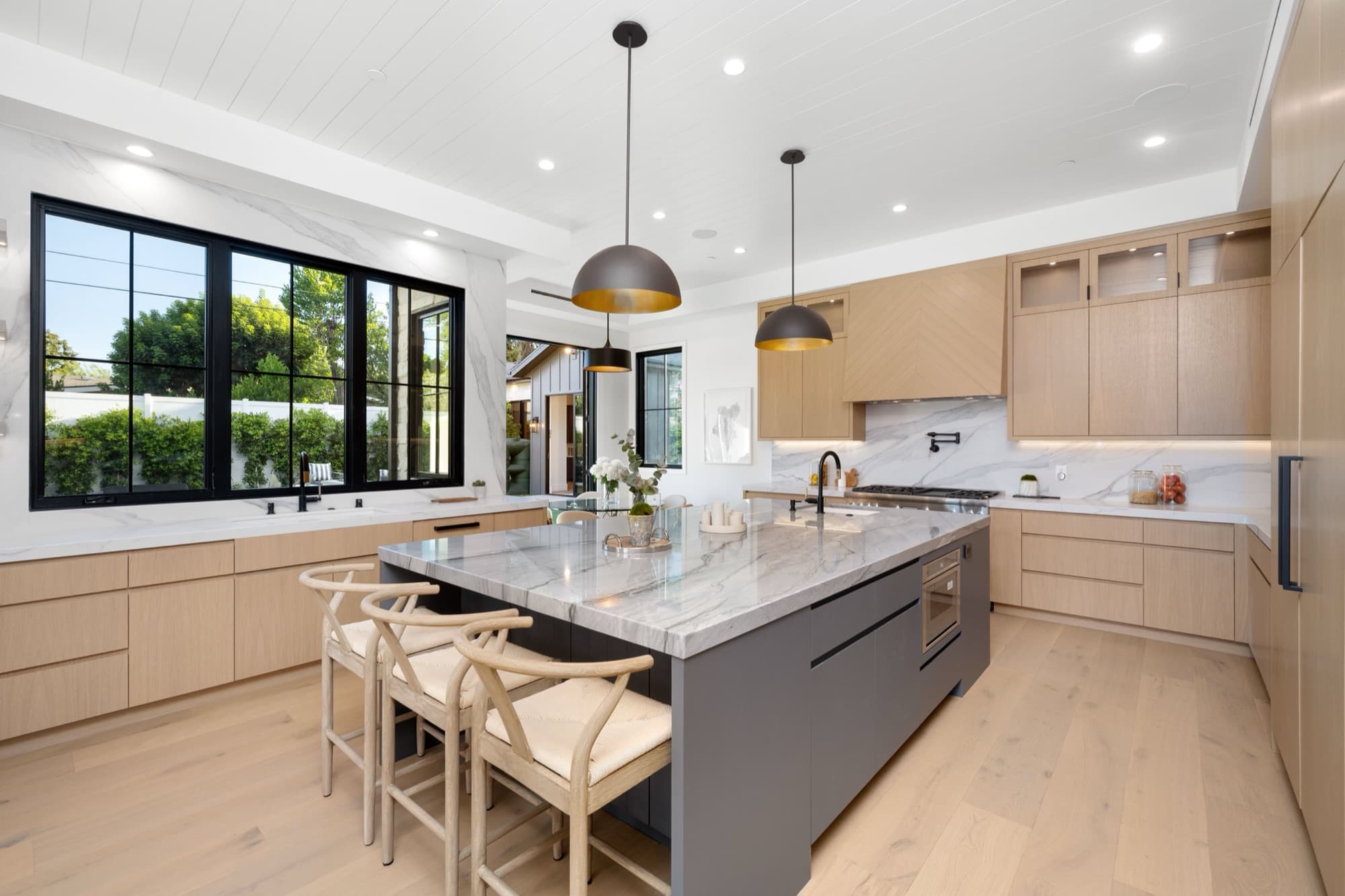 Open-plan kitchen with a marble-topped island, pendant lighting and light oak cabinetry