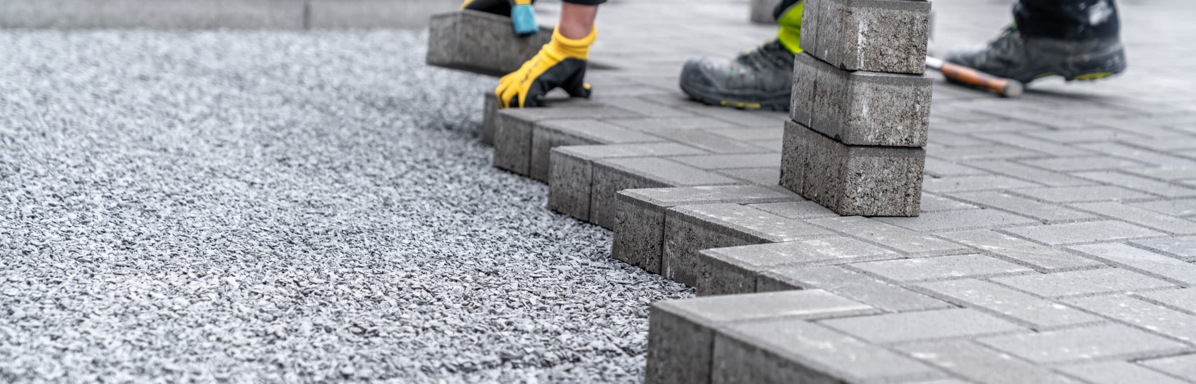 Block paving being laid onto a compacted sub-base, with a stack of pavers and a laying course of gravel
