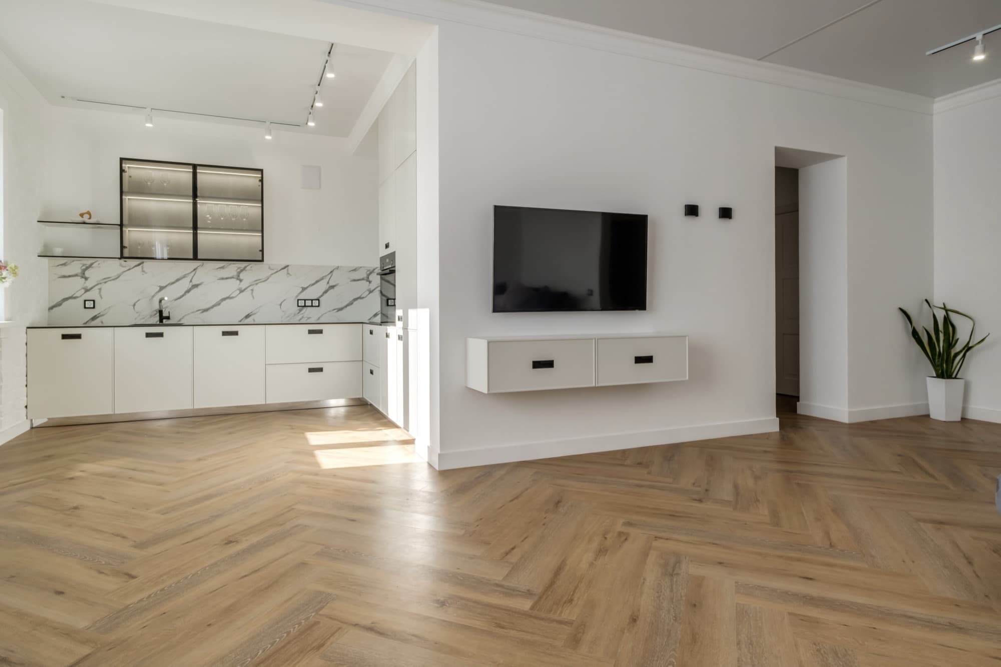 Herringbone floor running through an open-plan kitchen and living space with a marble splashback